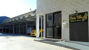 Un edificio con estacionamiento techado, un auto amarillo en su interior, y un letrero de bienvenida al Motor Inn Siesta Villa.