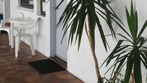 Una habitación con una pared blanca, una planta en maceta, una ventana y una silla blanca.
