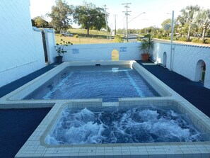 A rectangular hot tub with a tiled border, surrounded by a white wall with a tiled pattern.