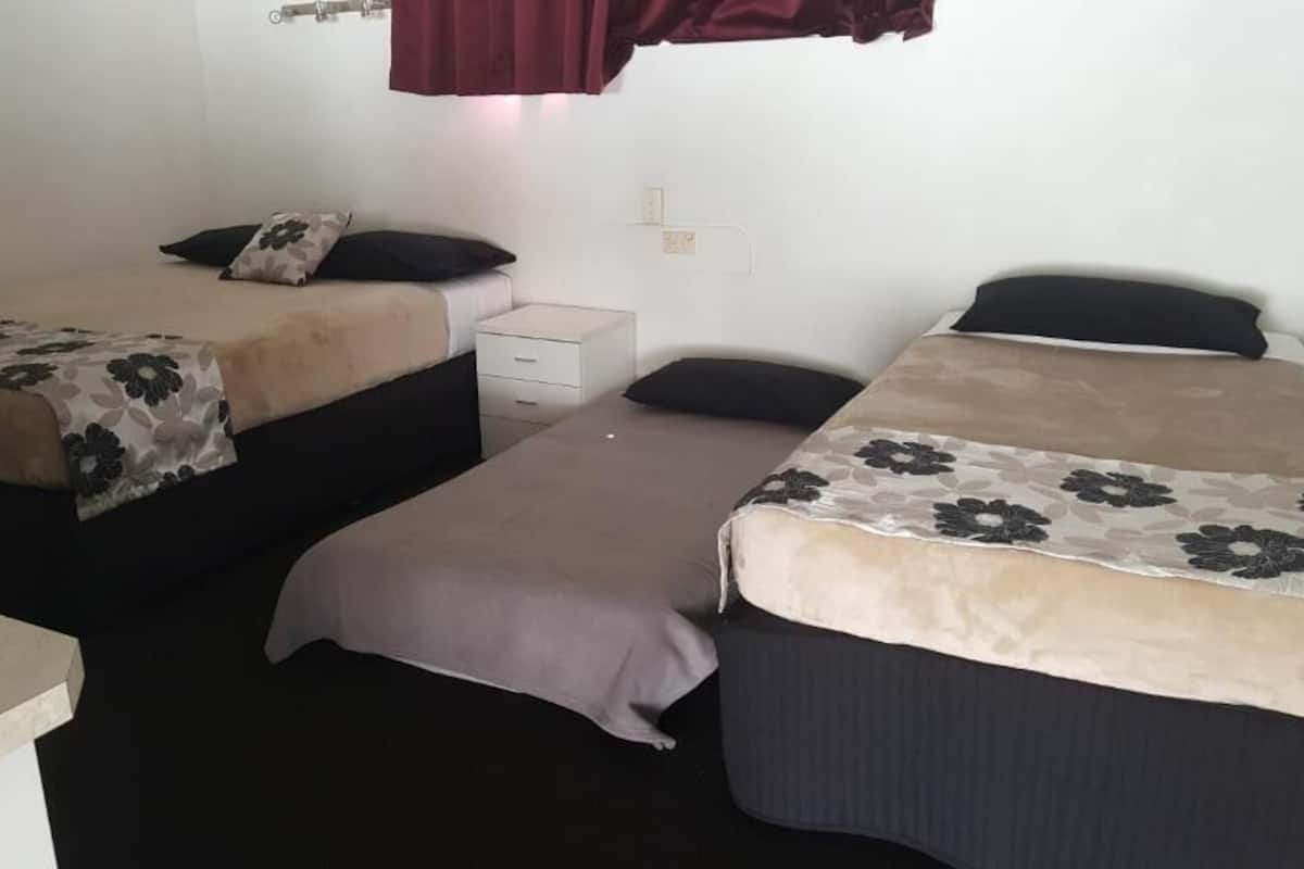 A room with two single beds, each with a floral-patterned bedspread and a pillow. There is a small white bedside table between the beds.