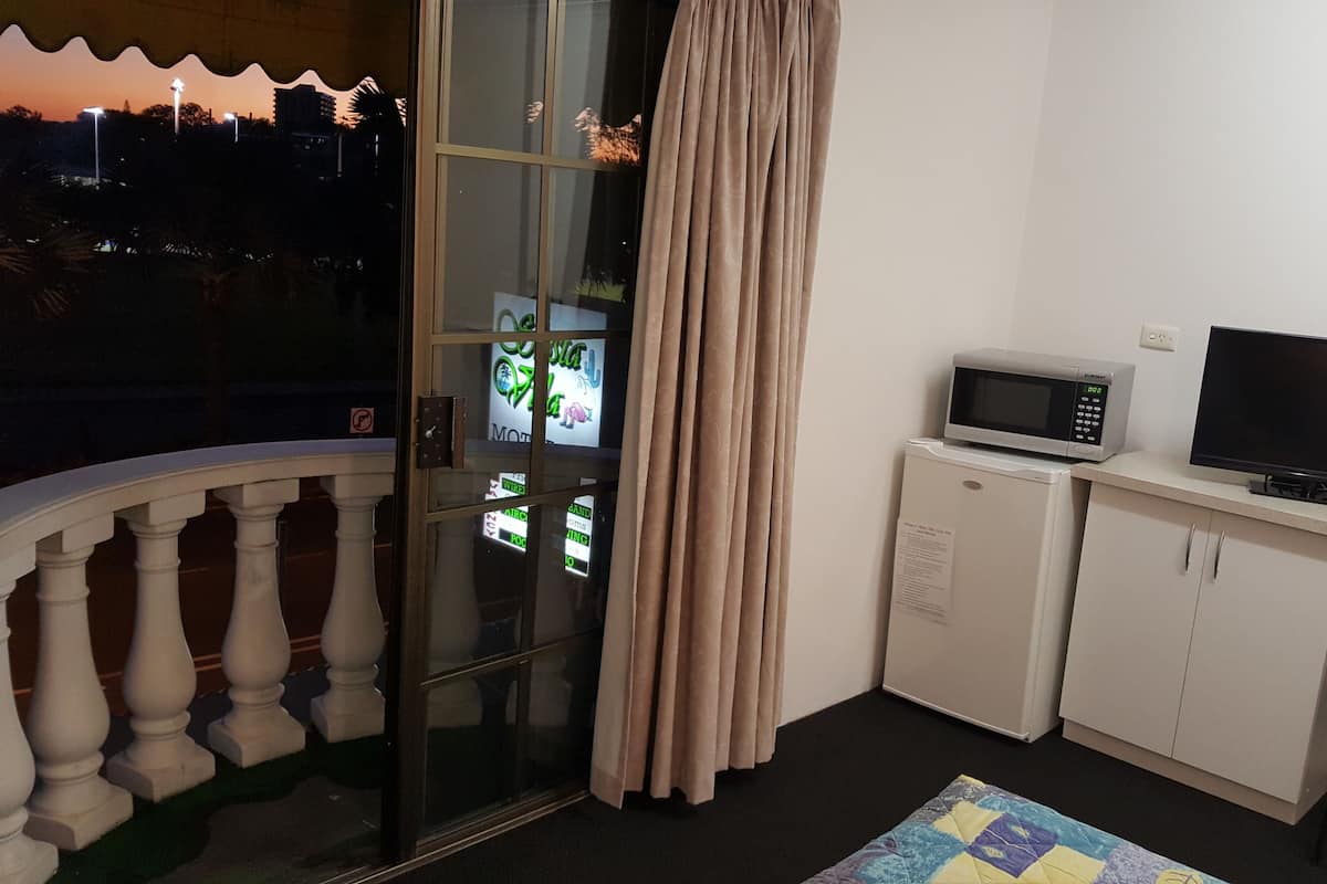 A room with a balcony, a sliding glass door with curtains, a microwave, a television, and a small cabinet.