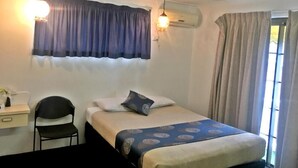 Un dormitorio con cama, escritorio, silla, equipo de aire acondicionado y ventana con cortinas.
