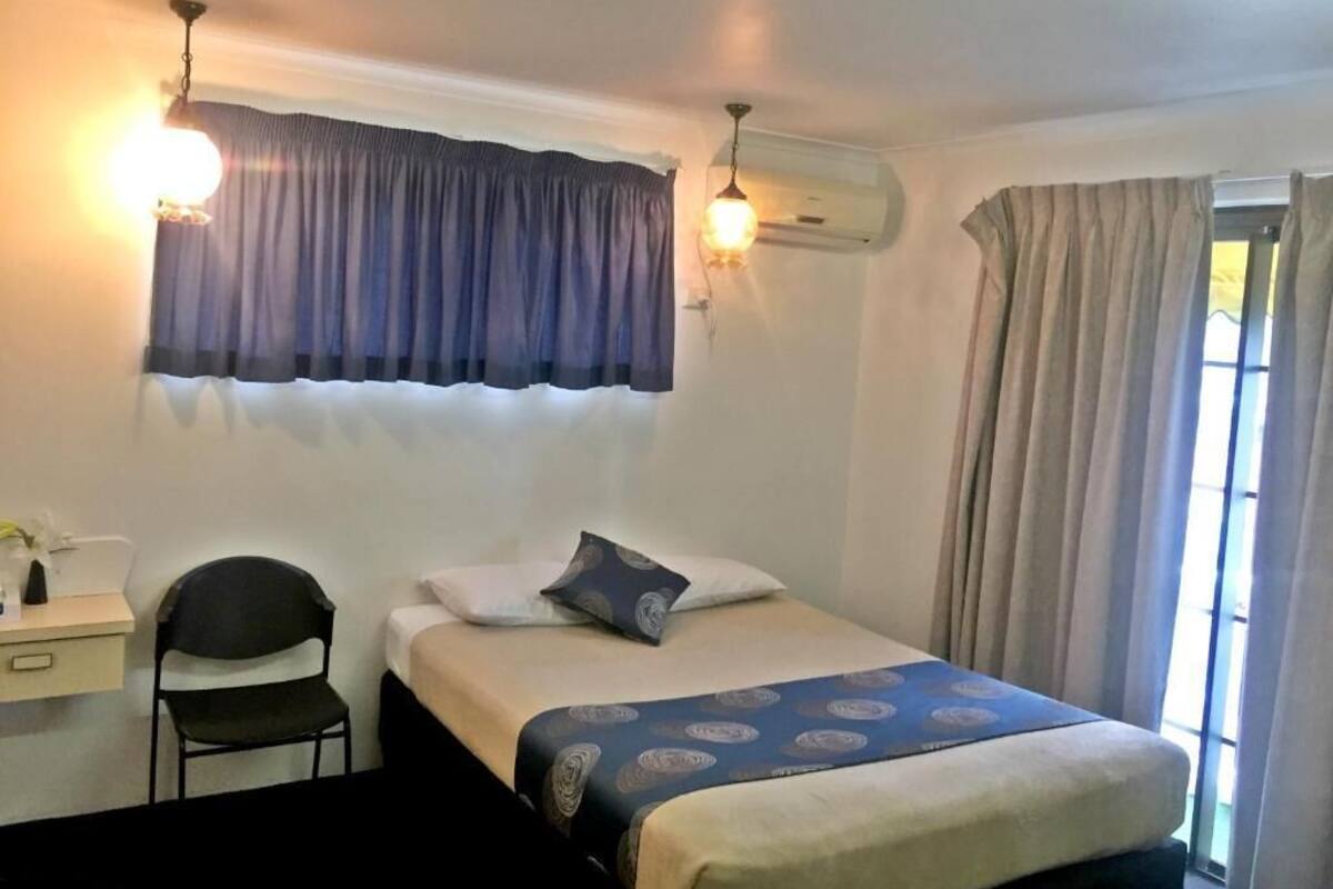 A bedroom with a bed, a desk, a chair, an air conditioning unit, and a window with curtains.