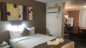 A hotel room with a bed, a bedside table with a tissue box, a wall-mounted air conditioner, a desk with a lamp, and a chair. - Riverview Motor INN Taree (Taree)