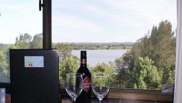 A bottle of wine and two glasses on a table with a view of a lake and trees. - Riverview Motor INN Taree (Taree)