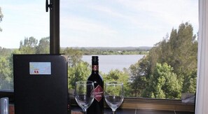Une bouteille de vin et deux verres sur une table, avec vue sur un lac et des arbres.