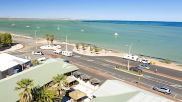 A coastal road with a roundabout, beachside shops, and a view of the sea.