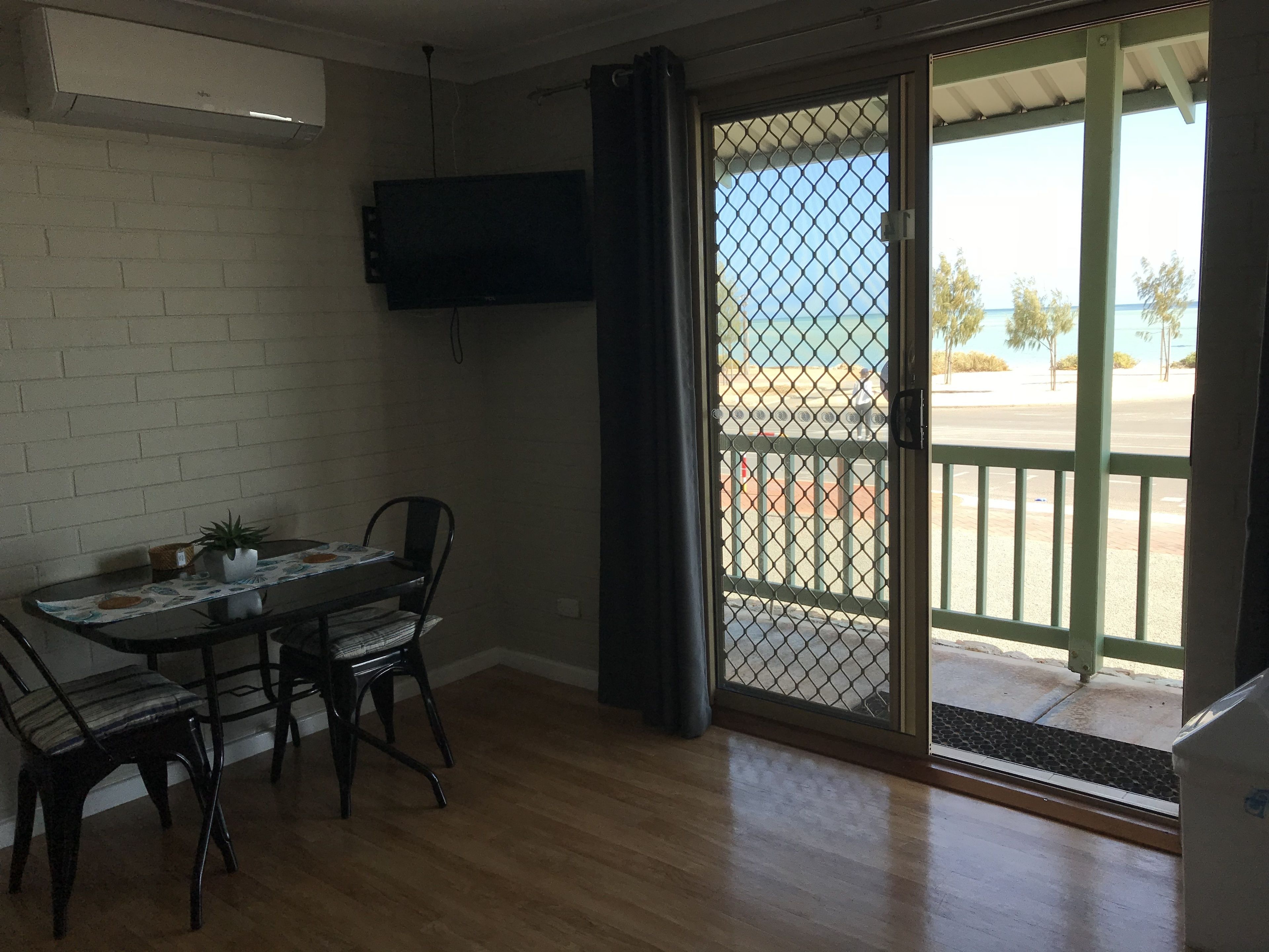 A room with a dining table, chairs, a TV mounted on the wall, and a sliding glass door leading to an outdoor area.