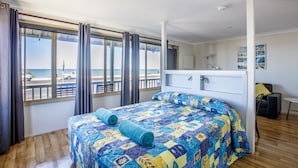 Un dormitorio con una cama grande, vista a la playa y un escritorio pequeño con una silla.
