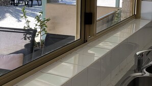 Vista desde una habitación con un ventanal grande que da a una zona de piscina con sillas de descanso y palmeras.