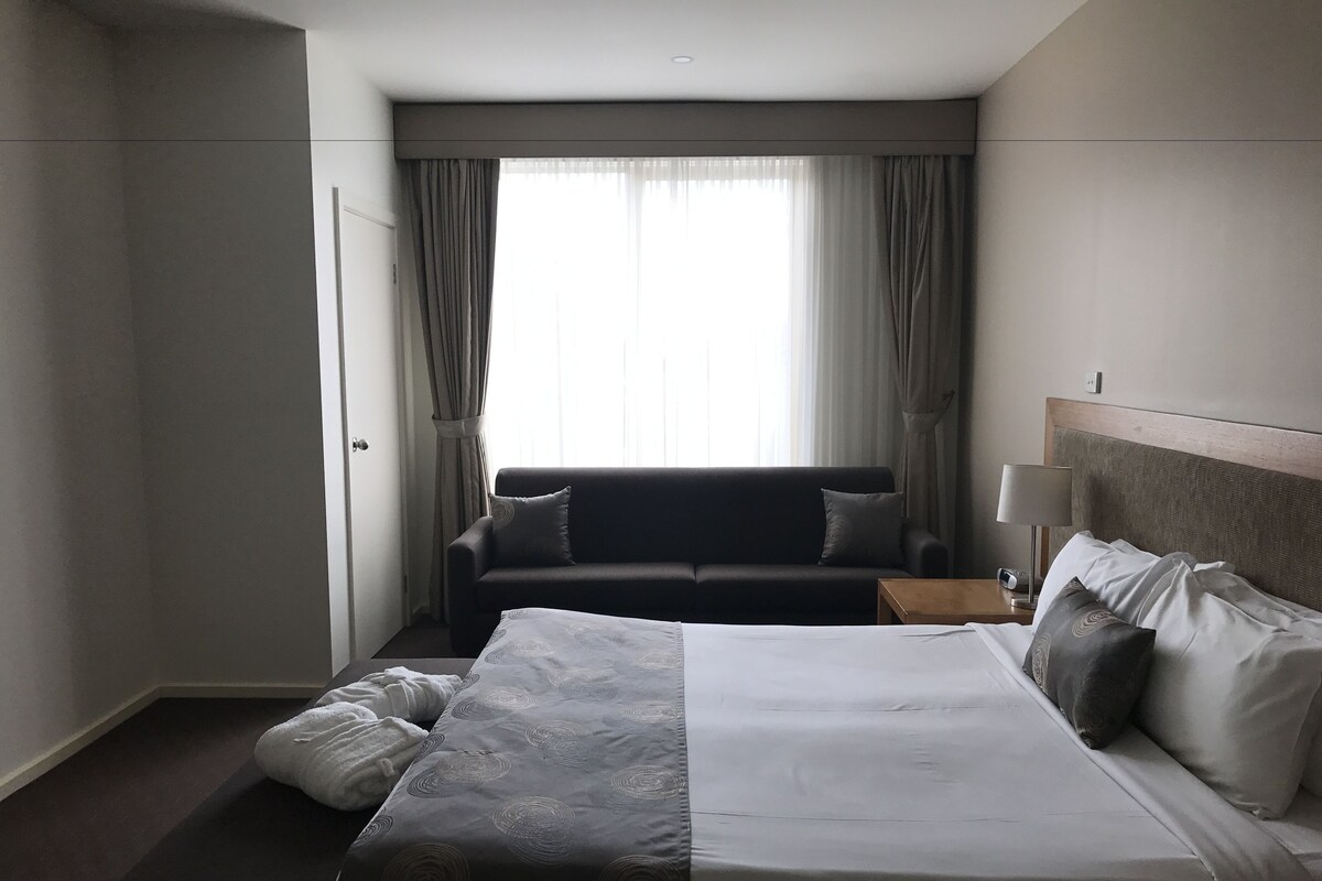 Una habitación de hotel con una cama, un sofá, una mesita de noche y una ventana con cortinas.