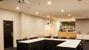 Un salón de conferencias con una larga mesa, sillas, una zona de bar y una puerta con la etiqueta 'EXIT'.