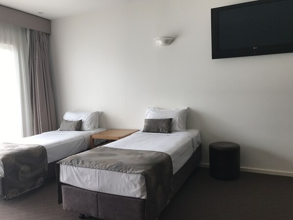 Habitación de hotel con dos camas, una mesita pequeña, un televisor montado en la pared y un cesto de basura.