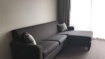 A dark-colored sofa with a matching ottoman and two pillows against a plain wall.