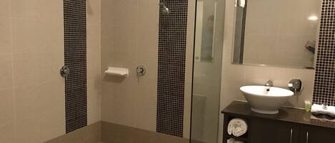 Et moderne badeværelse med glasvæg omkring brusebad, en hvid vask og et mørkt toiletbord.