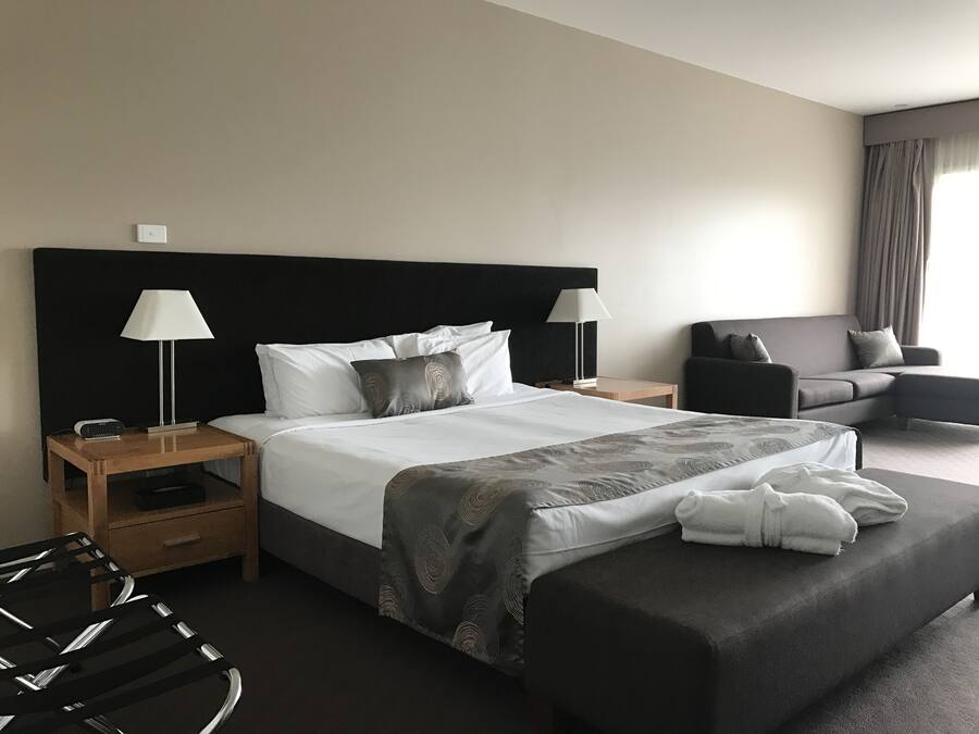 Una habitación de hotel con una cama grande, dos mesitas de noche, una silla y un sofá.