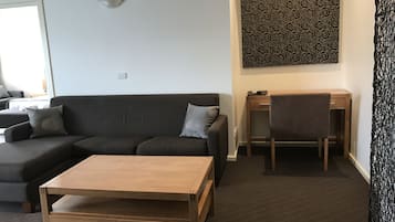 A modern living room with a dark grey sofa, a wooden coffee table, a desk with a chair, and a patterned artwork on the wall.