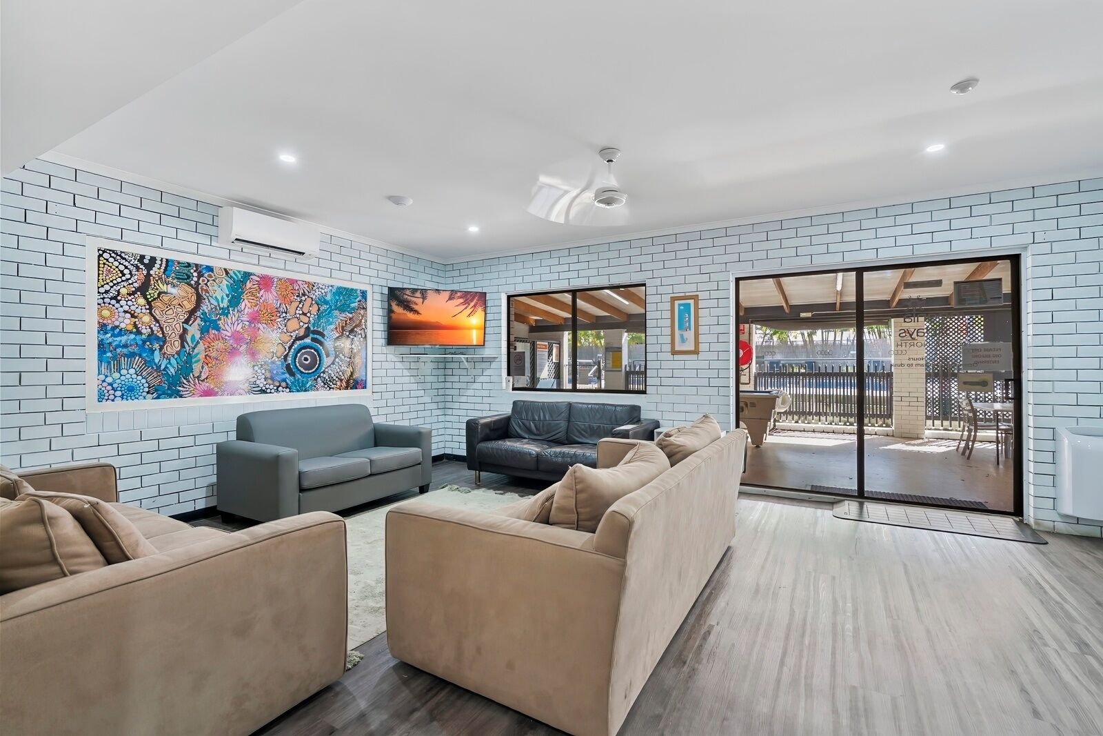 A modern living room with a brick wall, a large abstract painting, a flat-screen TV, and a sliding glass door leading to an outdoor area.