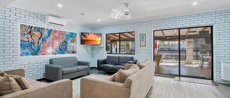 A modern living room with a brick wall, a large abstract painting, a flat-screen TV, and a sliding glass door leading to an outdoor area.