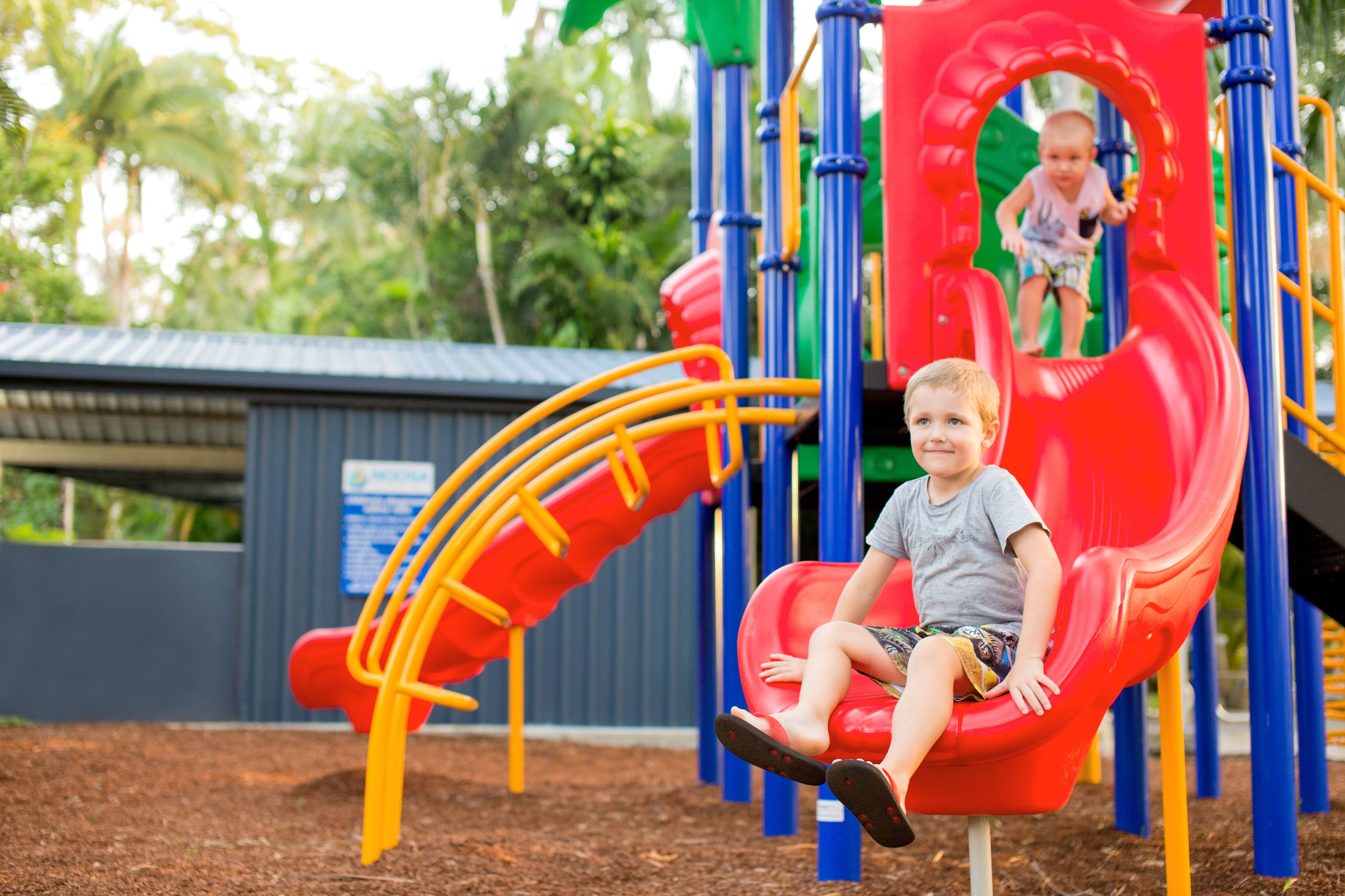 Un terrain de jeux avec un toboggan rouge et un enfant assis dessus.