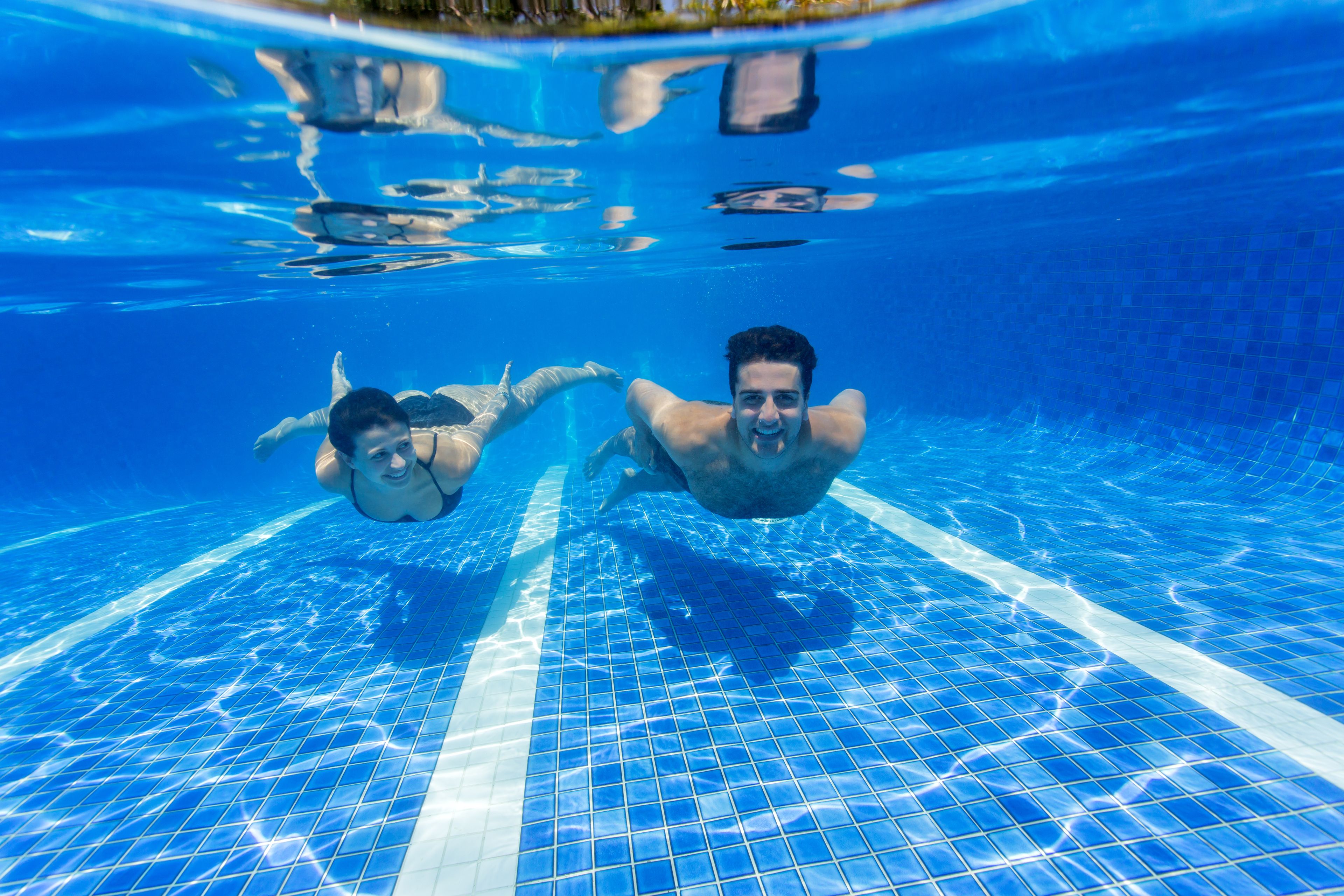 An underwater view of a swimming pool with clear blue tiles and visible reflections.