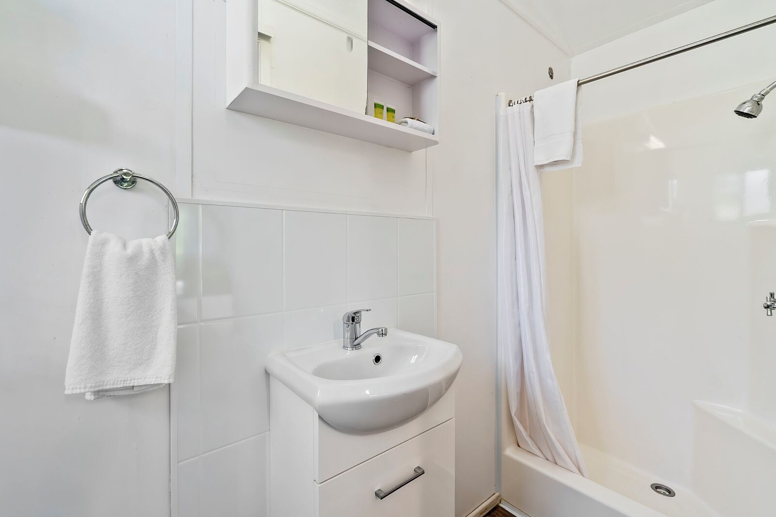 Uma casa de banho moderna com lavatório, espelho, chuveiro e um porta-toalhas.