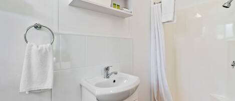 Uma casa de banho moderna com lavatório, espelho, chuveiro e um porta-toalhas.