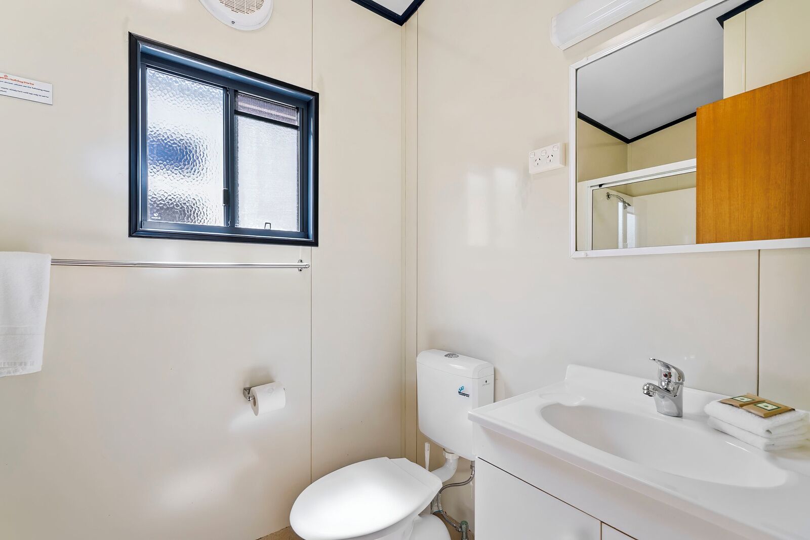 Ein Badezimmer mit Toilette, Waschbecken, Spiegel, Fenster und Handtuchhalter.