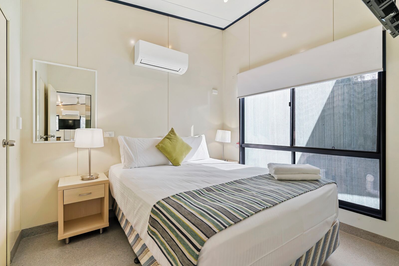 Hotelkamer met een bed, bedlampen, nachtkastje, spiegel, airconditioning en een groot raam.
