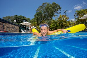 A swimming pool with clear blue water, surrounded by palm trees and a brick building. - Ingenia Holidays Noosa North (Tewantin)