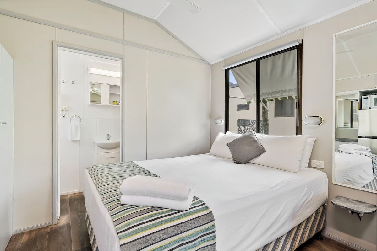Une chambre à coucher comprenant un lit, une table de chevet, un miroir, une fenêtre et une porte donnant sur une salle de bain.
