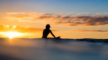La silhouette d’une personne assise sur une planche de surf, se détachant sur le ciel d’un coucher de soleil.