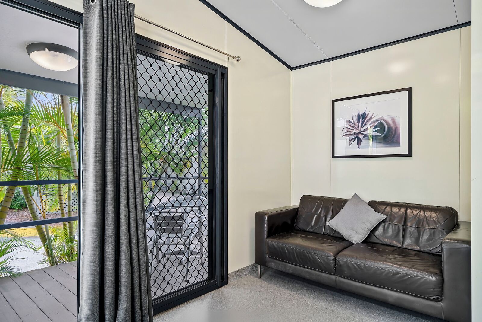A modern room with a leather sofa, a framed artwork, and a view through a mesh door.