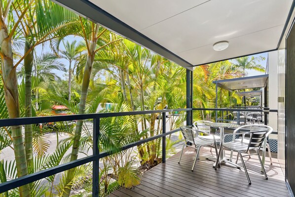 A balcony with a view of palm trees, a covered seating area, and a railing.