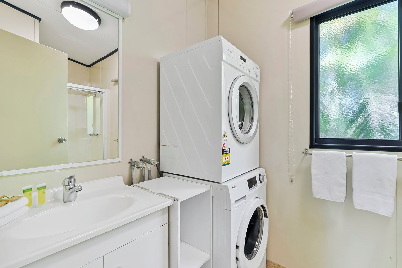 Bagno d'albergo con doppio lavabo, lavatrice, specchio e finestra vista.