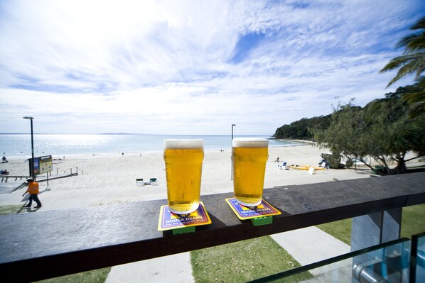 Two glasses of beer on coasters with a beach view in the background.