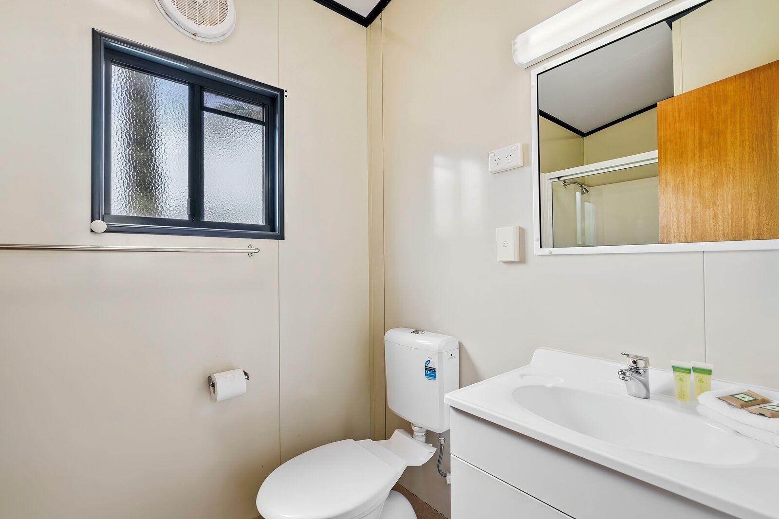 Un baño con inodoro, lavabo, espejo y ventana.