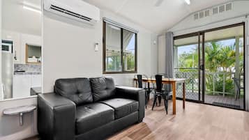 Een moderne woonkamer met een zwarte leren bank, een eettafel met stoelen, een keukenhoek en een schuifpui naar een balkon.