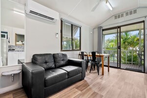 Un salón moderno con un sofá de cuero negro, una mesa de comedor con sillas, una zona de cocina y un ventanal corredero a un balcón.
