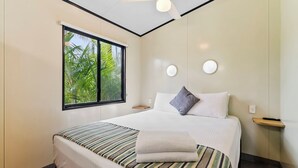Habitación de hotel con cama, ventana que ofrece vistas a zonas verdes, ventilador de techo y mesita de noche con lámpara.