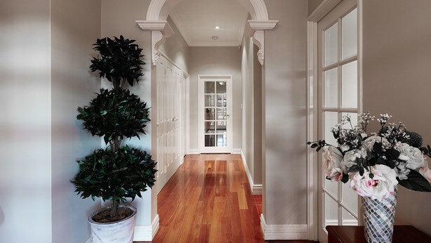 A hallway with a wooden floor, white walls, and a white door at the end. There are two potted plants on either side of the hallway.