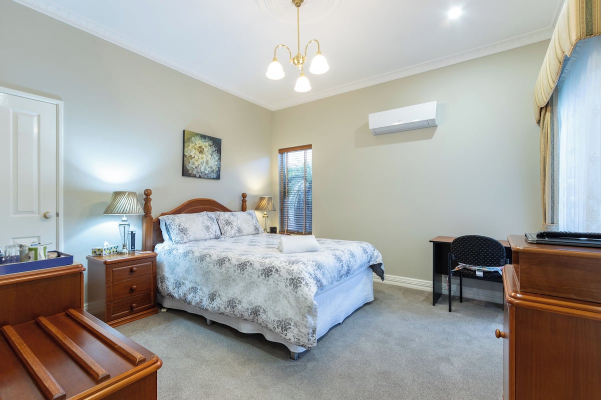 A bedroom with a bed, bedside table, lamp, and a window with blinds.