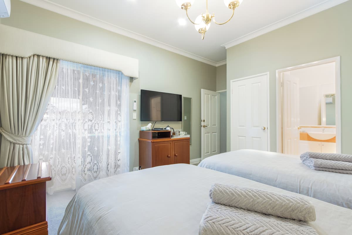 A hotel room with two beds, a wooden dresser, a flat-screen TV, and a chandelier.
