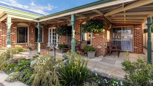 A brick house with a covered patio, outdoor seating, and a garden with various plants.