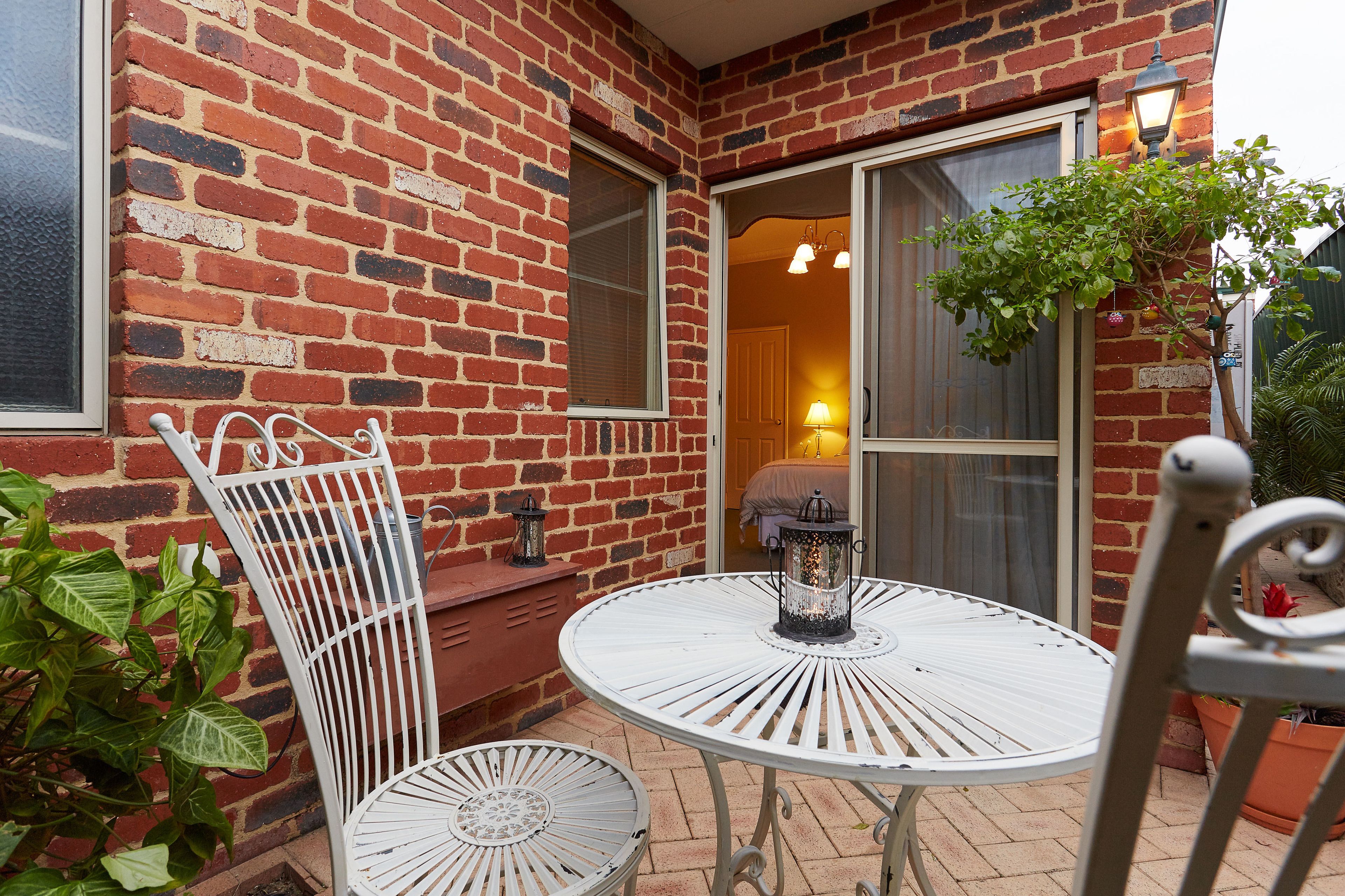 A patio with a round metal table and two metal chairs, a brick wall, and a door leading inside.