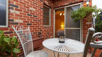 A patio with a round metal table and two metal chairs, a brick wall, and a door leading inside.