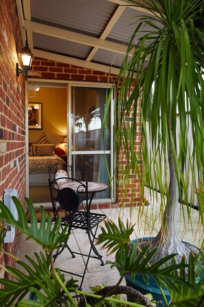 A patio with a table and chairs, a potted plant, and a view of a bedroom through a glass door. - Durham Lodge (Victoria Park)