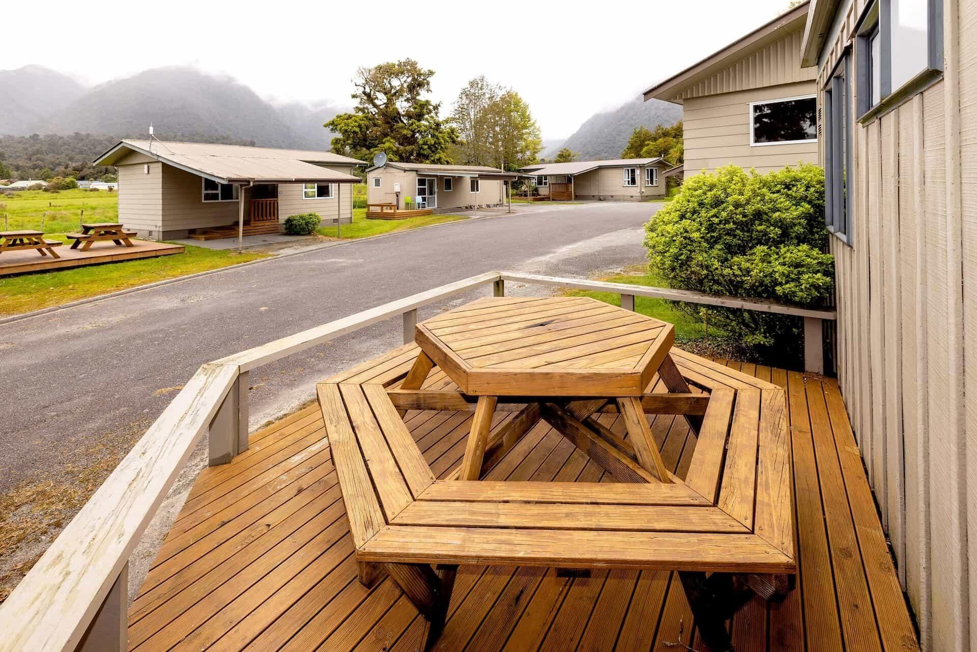 A wooden deck with a table and benches, overlooking a road with several buildings in the background.