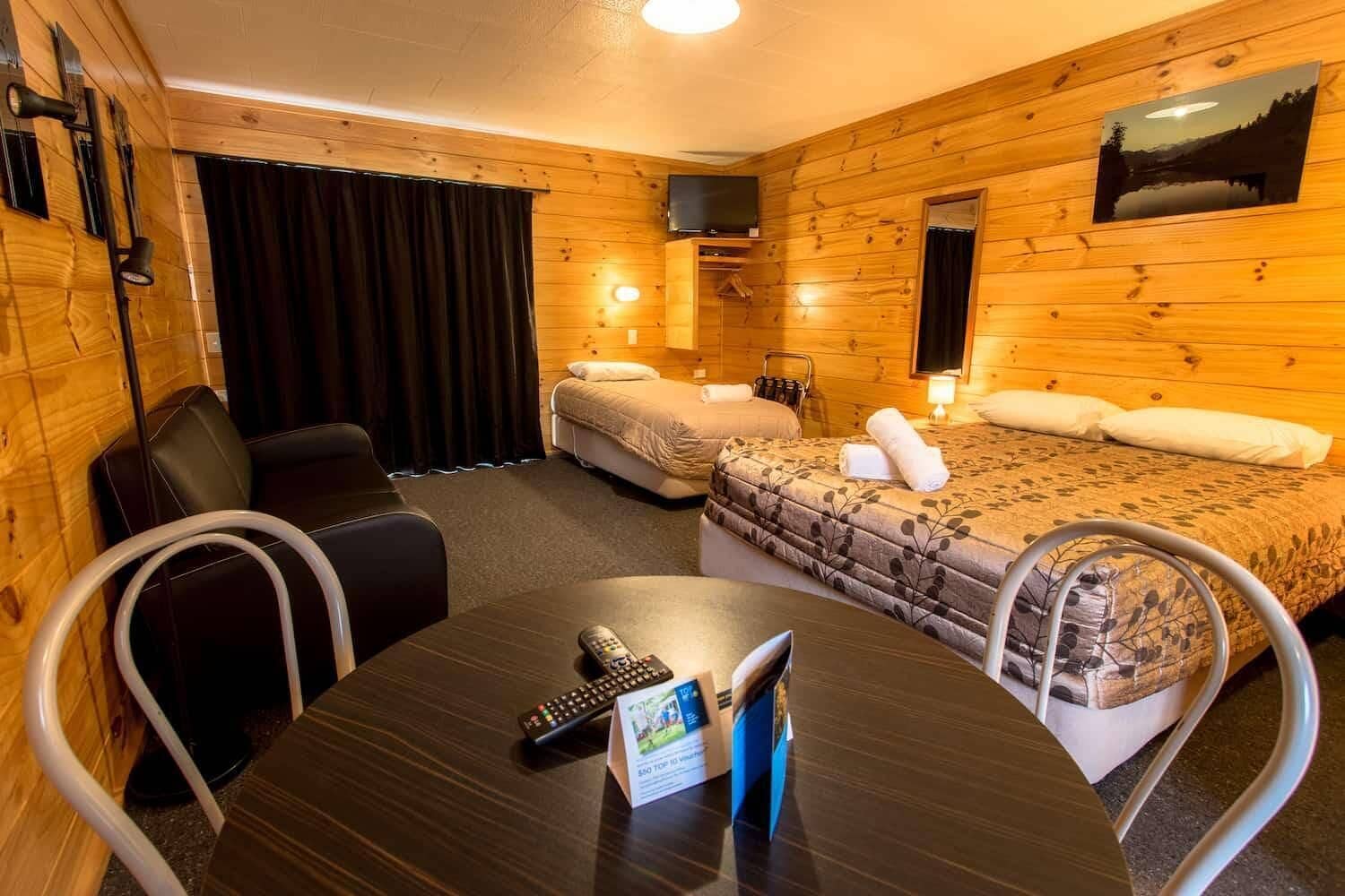 A cozy room with wooden walls, a bed, a desk with a remote control, and a TV.