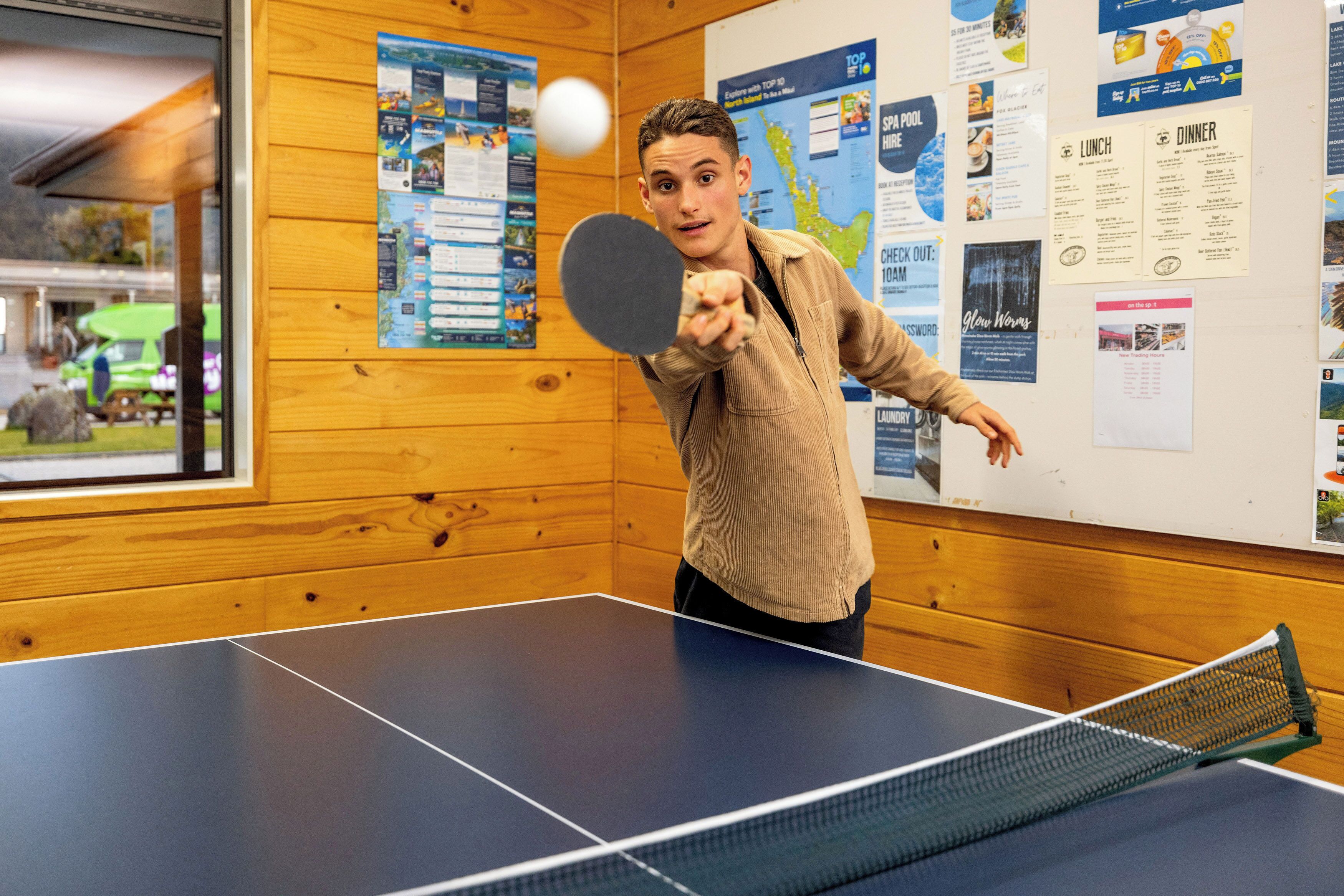 Una mesa de ping pong en una habitación con paredes de madera, rodeada de varios carteles informativos.